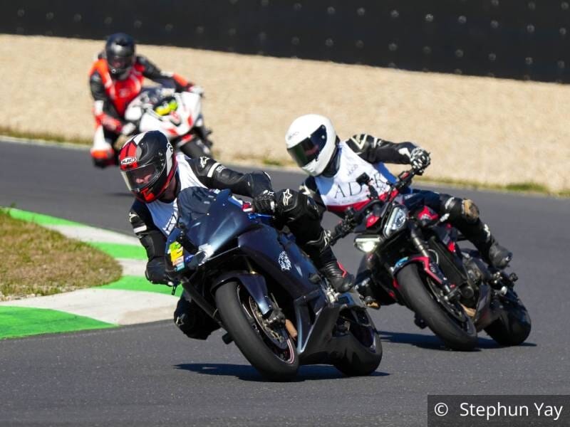 Trois pilotes de moto sur un circuit, dans un virage, deux au premier plan et un au second